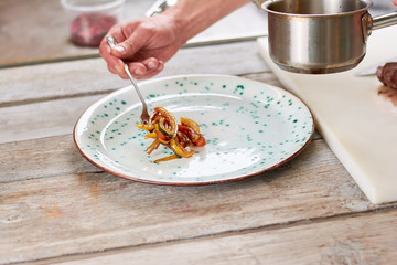 Chef putting vegetables from saucepan on plate. Male chef putting garnishing from vegetables on plate.