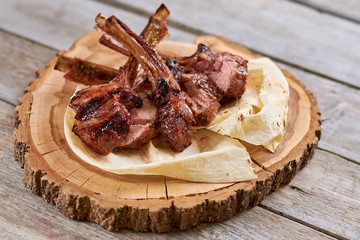 Appetizing roasted ribs calf on natural wood. Grilled ribs with lavash on wooden stand. Delicious meat on wooden table.