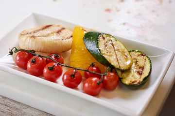 Glilled vegetables on plate close up. Grilled cherry tomatoes, zucchini, pepper and onion on white porcelain plate. Delicious vegetarian food.