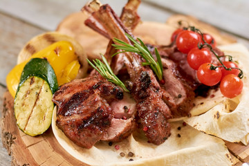 Roasted calf ribs with grilled vegetables. Juicy calf ribs with cherry tomatoes, zucchini, pepper and onion close up.