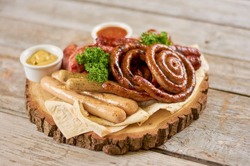 Appetizing grilled sausages in restaurant. Assortment of tasty sausages with mustard and parsley on wooden table.