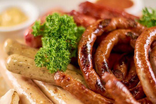 Appetizing grilled sausages with parsley. Assortment of delicious fried sausages close up. Tasty food of european restaurant.