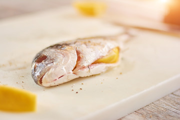Raw fish prepared with salt and spices. Raw fish with lemon inside on kitchen board close up. Cooking dorado fish.