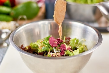 Sauce pouring in bowl with mixed salad. Green healthy salad in stainless bowl in restaurant. Chef...
