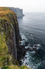 Mealt Falls and Kilt Rock cliff in the coast near Portree, in the Isle of Skye, Scotland. The waterfall plunges into the sea with the basalt column formation resembling a skirt in the background.