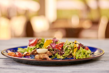 Quail with green salad on blue plate. Appetizing warm salad with quail carcass and meat on blurred background.