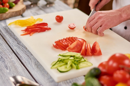 The process of cutting vegetables on white board. Male chef hands chopping fresh vegetables on cutting board. Chef working at professional kitchen.