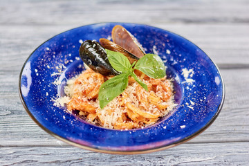 Pasta served with mussels and fresh basil. Delcious pasta with seafood and parmesan on blue porcelain plate.