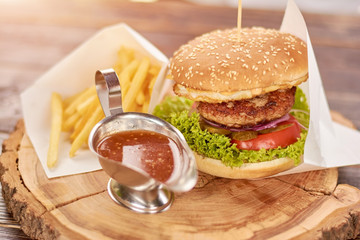 Appetizing burger with double meat. Delicious burger with french fries and sauce on wooden board. Tasty dinner in restaurant.