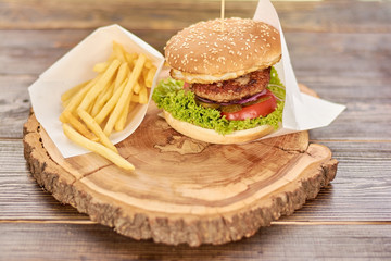 Hamburger with fresh vegetables and meat. Burger with beef, tomato, lettuce, pickled cucumbers. Cheesburger on rustic wooden background.