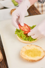 Chef adding tomatoes on burger. Cook preparing hamburger at professional kitchen. Cooking and cuisine concept.