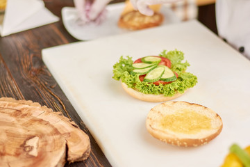 Hamburger making at kitchen. Bun for hamburger with fresh lettuce, tomatoes and cucumbers.