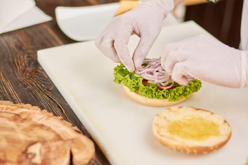 Chef hands adding onion on burger. The process of cooking fresh delicious hamburger at kitchen by chef. Chef working at kitchen.