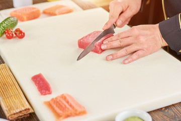 Obraz na płótnie Canvas Chef cutting raw tuna on cutting board. Cook hands with knife slicing fresh fillet of tuna for making sushi. Chef at work, kitchen.