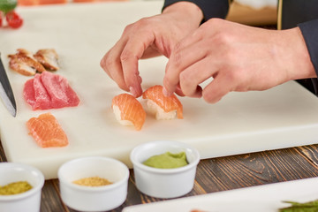 Chef hands cooking nigiri sushi. Male chef hands preparing nigiri sushi with salmon on white board. The process of sushi making.