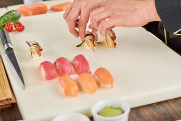 Chef hands putting sushi with eel on white board. Chef cooked sushi with eel. Chef at kitchen cooking nigiri sushi with salmon, tuna and eel.