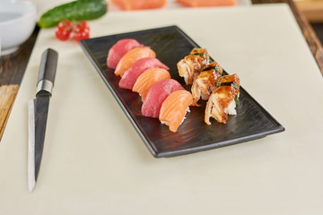 Fototapeta na wymiar Slices of appetizing sushi on plate. Delicious sushi nigiri with salmon, tuna and eel at kitchen of restaurant. Knife, sushi, cutting board.