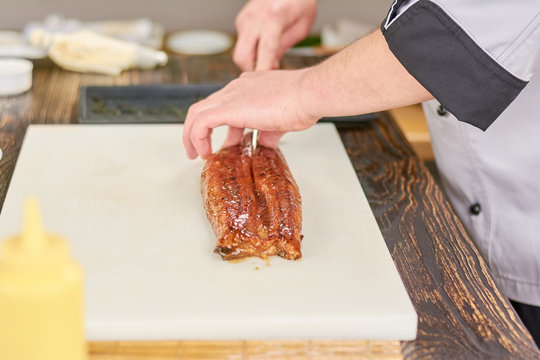 Chef hands slicing eel on cutting board. Male hands cutting fresh eel on white cutting board. Chef at work, kitchen.