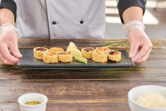 Chef hands holding plate with sushi rolls. Unagi sushi rolls on traditional japanese dish in cook hands. Sushi with eel and avocado.