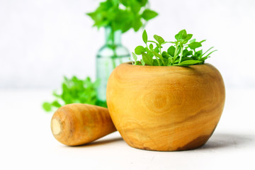 Green lemon basil in a wooden mortar on a light background. Behind the basil in the bottle.