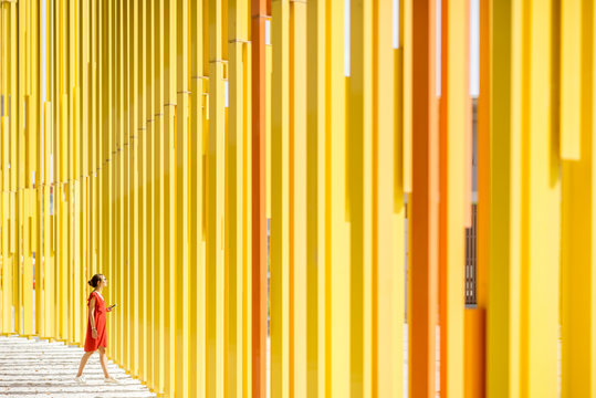 Fototapeta Woman in red dress on the modern yellow building wall background. General plan with abstract geometric composition