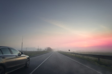 summer rural landscape with blue and red sky, fog and the road. sunrise. Dark car is moving to the sun