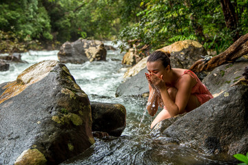 Fototapeta na wymiar the girl drinks water from a mountain stream