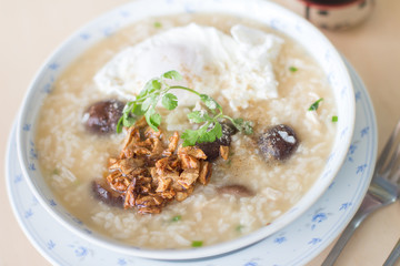 Rice porridge with garlic and egg breakfast in white bowl on wooden table