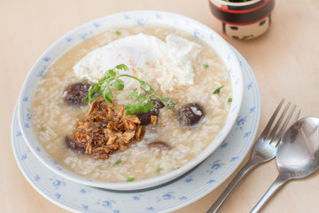 Rice porridge with garlic and egg breakfast in white bowl on wooden table