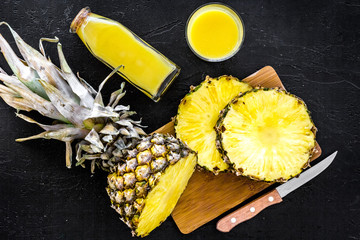 Freshly squeezed pineapple juice near fruit slices on black background top view