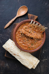 Clay bowl of soup kharcho served with lavash, above view on a dark brown stone surface