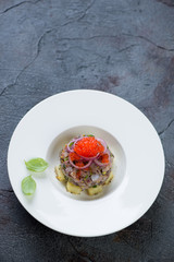 Herring tartar with red caviar and potato served in a white plate, grey stone background with space, vertical shot