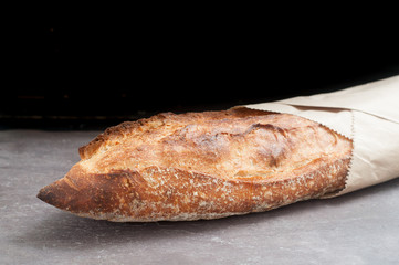 Rustic sourdough baguette served wrapped in paper on a grey slate counter top.