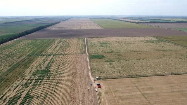 An amazing bird`s eye view of a colorful agricultural field with several cars on it on a sunny day in summer. The skyscape is light blue and impressive. The field is weel groomed.