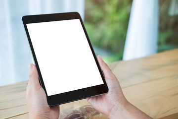 Fototapeta na wymiar Mockup image of hands holding black tablet pc with blank white screen on wooden table in cafe