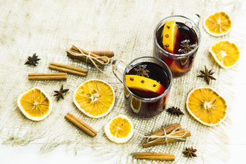 two transparent cups with hot mulled wine and an orange slice among spices of cinnamon and anise