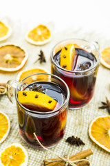 two transparent cups with hot mulled wine and an orange slice among spices of cinnamon and anise