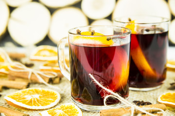 two transparent cups with hot mulled wine and an orange slice among spices of cinnamon and anise