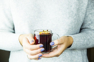 a girl in a gray sweater is holding a cup of hot mulled wine with an orange slice