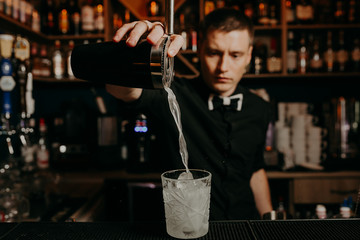 Young handsome Barman in bar interior mixing alcohol cocktail. Professional bartender at work