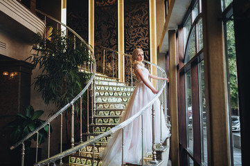 Beautiful bride in a white dress with a long train goes up the spiral staircase.