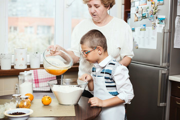 Grandson helping his grandmother with baking, mixing wet and dry ingredients.