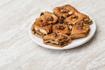 Oriental sweets baklava with honey and nut on white plate. Tasty oriental dessert on wooden background with copy space