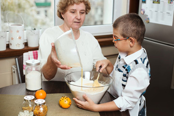 Grandson helping his grandmother with baking, mixing wet and dry ingredients.
