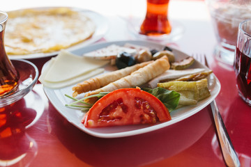 Plate with vegetarian food - bread roll with fresh vegetables cheese and olives next to glass with drink on red cafe table