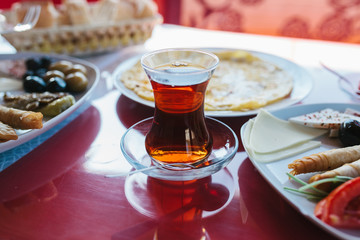A cup of hot fragrant black tea. Two plates with vegetarian food - fresh vegetables and cheese, cake and drink in glass on red table
