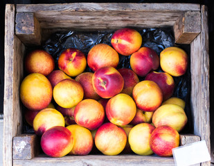 bunch of juicy delicious red yellow peaches prunus persica in a brown wooden box at the market