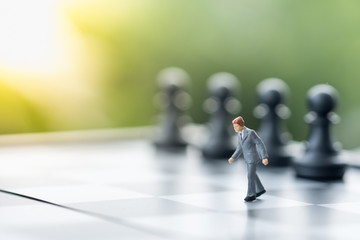 Business, target, decision and competition concept. Two businessman miniature figure walking on chessboard go to row of black chess pieces.