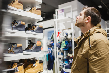 Man hipster in beige jacket choosing yellow winter boots in store - shopping, fashion, sale, ,style and people concept