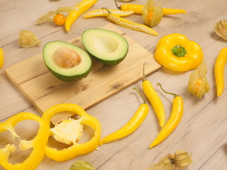 Organic food composition on the wooden table. Healthy vegetarian food on the white wooden background. Fresh and rape avocado, yellow paprika and chili peppers. Organic rape avocado in the kitchen.